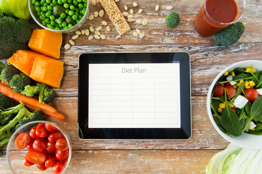 Close up image of tablet with diet plan on wooden table surrounded by healthy foods