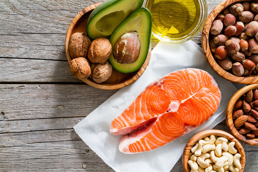 Healthy fat sources including salmon, nuts, and avacado on wooden table.